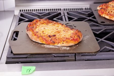 a pizza on a pizza steel on top of a gas oven