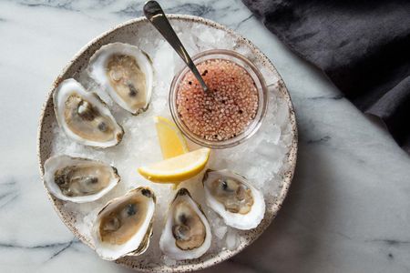 Overhead shot of bowl of oysters with mignonette and lemon wedges