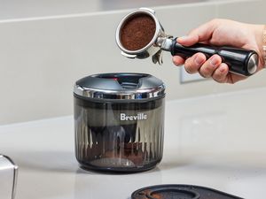 A person about to place a portafilter with espresso grounds in it into the Breville Puck Sucker.