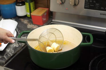 a spider strainer being used to deposit sliced plantains into hot oil