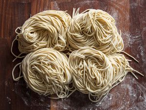 Freshly cut homemade ramen noodles in four nests on a flour-dusted wood surface