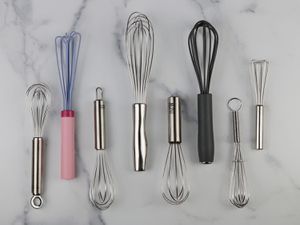 eight different miniature whisks on a marble background