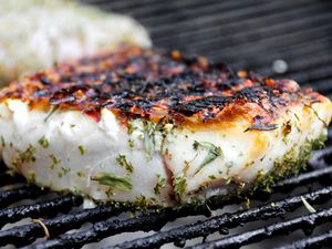 A fish fillet seasoned with herbs being cooked on the grill. 