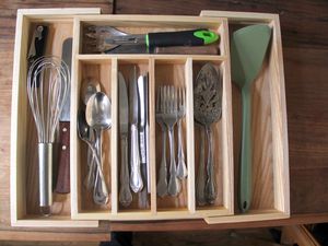Kitchen utensils and flatware in a wooden drawer organizer. 