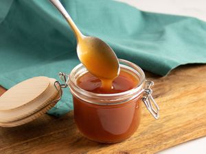 A spoon being pulled out of a glass jar of sweet and sour sauce.