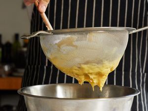Pastry cream being strained through a fine mesh strainer into a stainless steel bowl