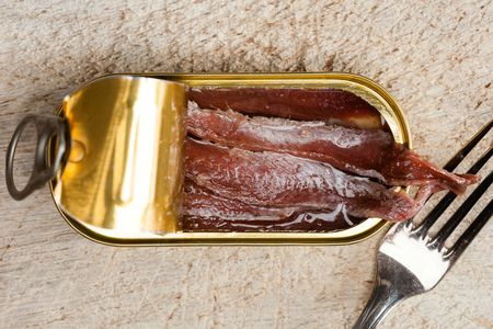 Overhead view of a tin of anchovies, partially opened to reveal the fillets inside.