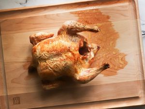 A roast chicken sitting in the center of a wooden carving board