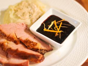 A plate of sliced ham and mashed potatoes with a white serving dish of Cumberland sauce.