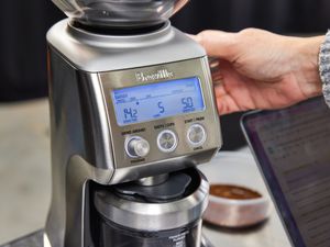 Person's hand touching the Breville The Smart Grinder Pro Coffee Bean Grinder displayed on a stainless steel surface