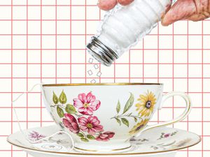 Table salt being added to a porcelain teacup covered with flowers.