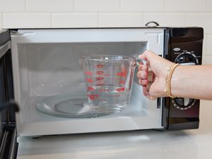 hand putting water in a measuring glass into the microwave
