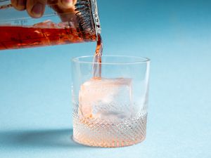 a cocktail being poured over a large ice cube in a rocks glass