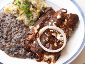 A plate of enchiladas served with mole aproximado, black beans, and rice. 