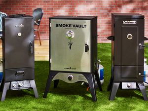 Three propane smokers sit side-by-side in a backyard.