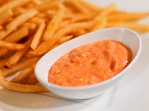 A small dish of sun-dried tomato and roasted garlic mayo next to a plate of French fries. 