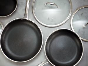 three hexclad skillets in different sizes with lids on a gray surface