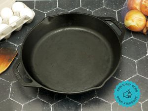 the lodge dual handled skillet on a black tile surface with a carton of eggs to the left and a bag of yellow onions on the right