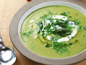 A bowl of cream asparagus and tarragon soup chopped tarragon,fennel frond, asparagus tips, a drizzle of olive oil, and a touch of crème fraîche.