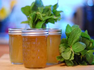 Profile view of several half-pint jars of mint jelly, flanked by bunches of fresh mint.