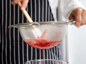A fine mesh strainer straining strawberry sauce