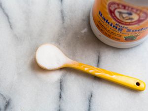 A small spoon holding baking soda with a container of baking soda next to it.