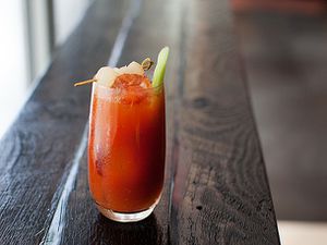 A Bloody Mary cocktail in a tall glass garnished with a celery stick and some shrimp on a toothpick. 