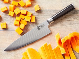 a closeup of the shun chef's knife on a wooden surface with cut up butternut squash