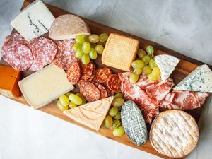 A charcuterie board with cheeses, sliced salami, and grapes on it.