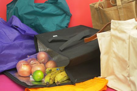 Numerous reusable grocery bags, with onions, a lime, and bananas spilling out of one.