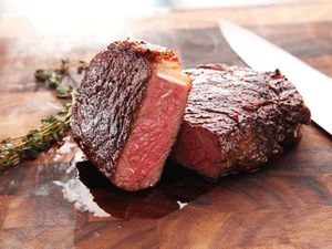 A seared rare steak cut in half on a wooden board