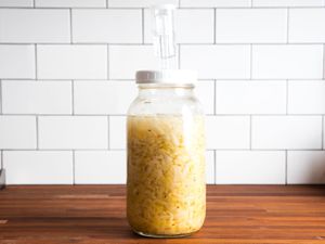 A jar full of sauerkraut on a countertop, with an airlock fixed on top to let gas out.