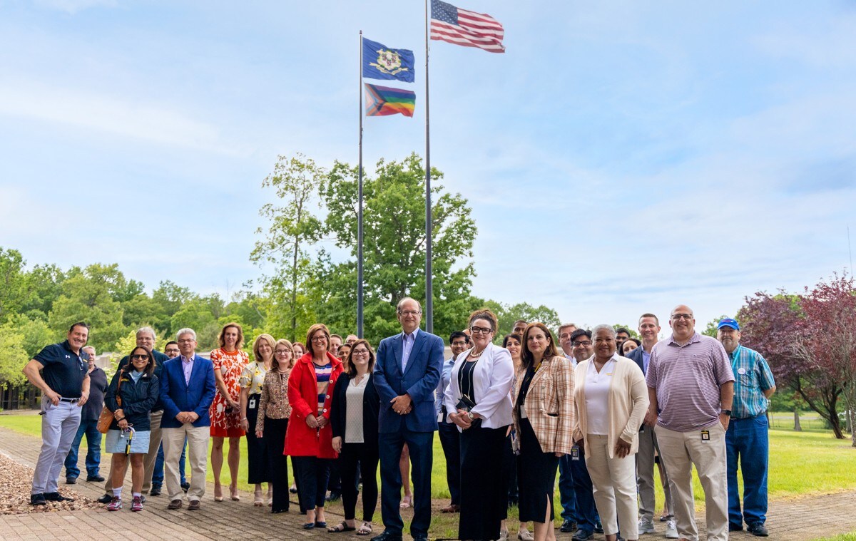 A large group of Stanley Black & Decker employees posing for a photo in front of flag poles outside of the World Headquarters