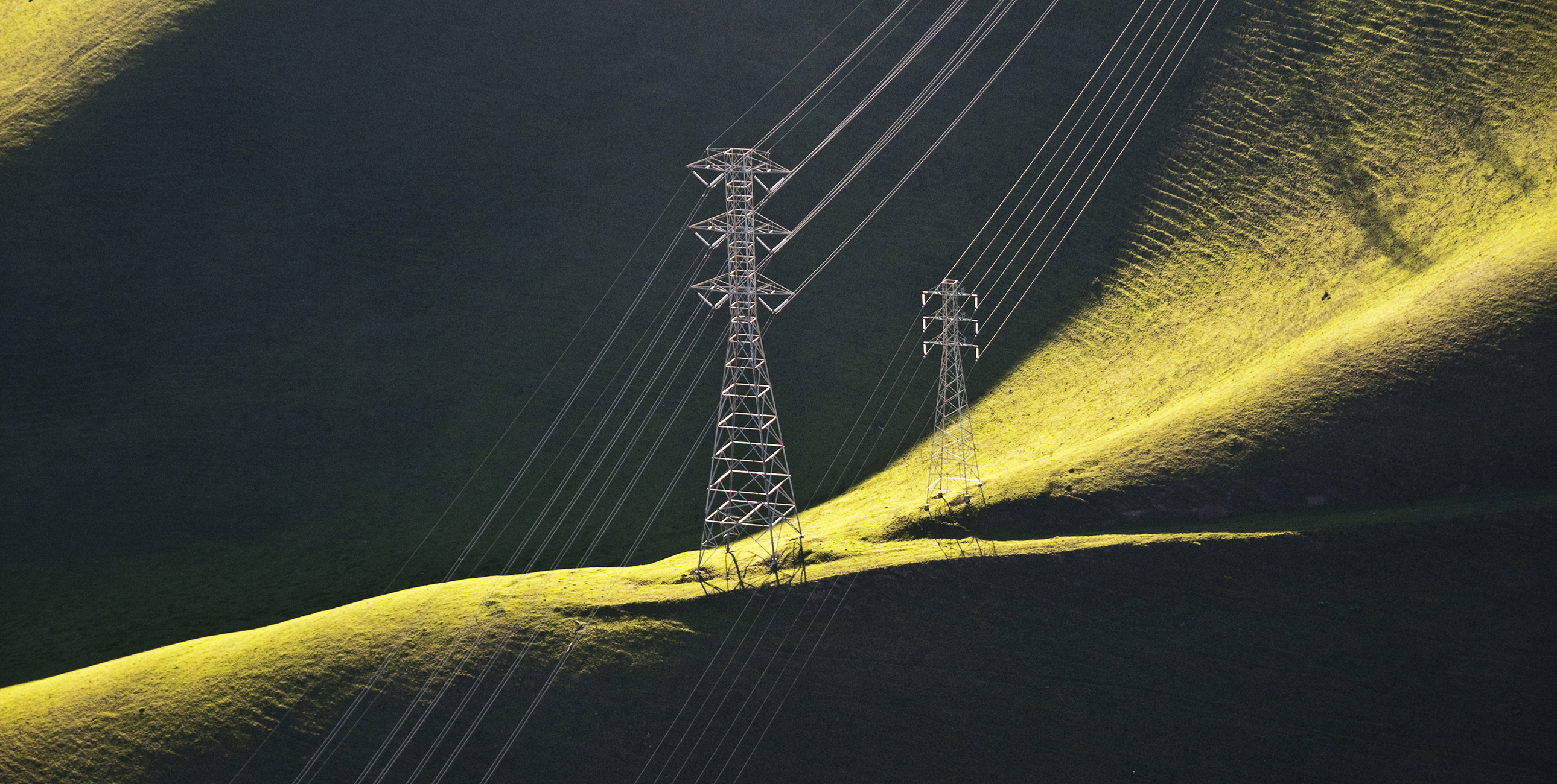 Transmission lines run across green hills.