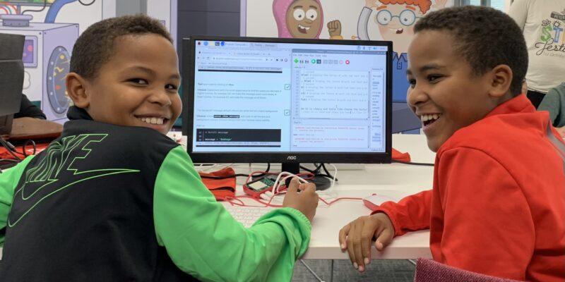 Two children at a coding club with their code on screen.