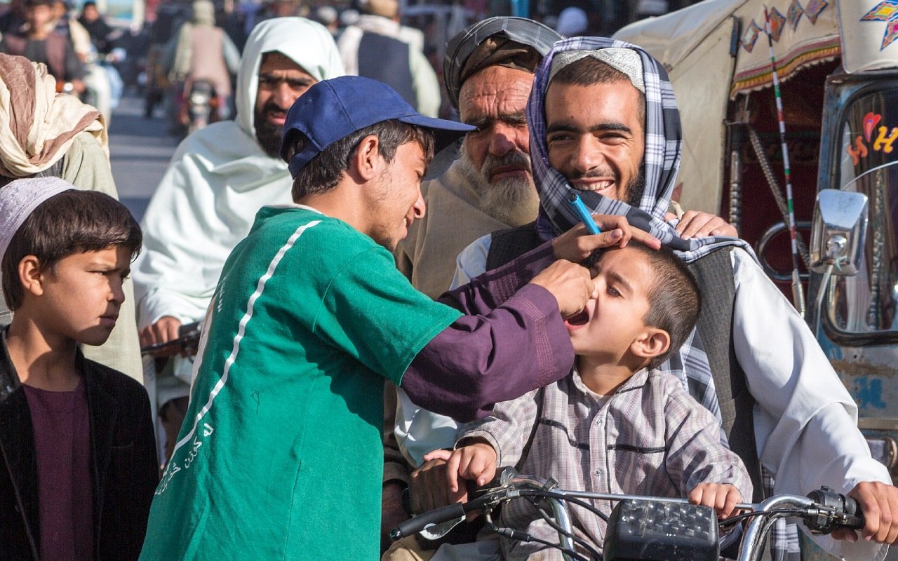 Volunteer vaccinating a Afghan boy against Polio on a busy street.
