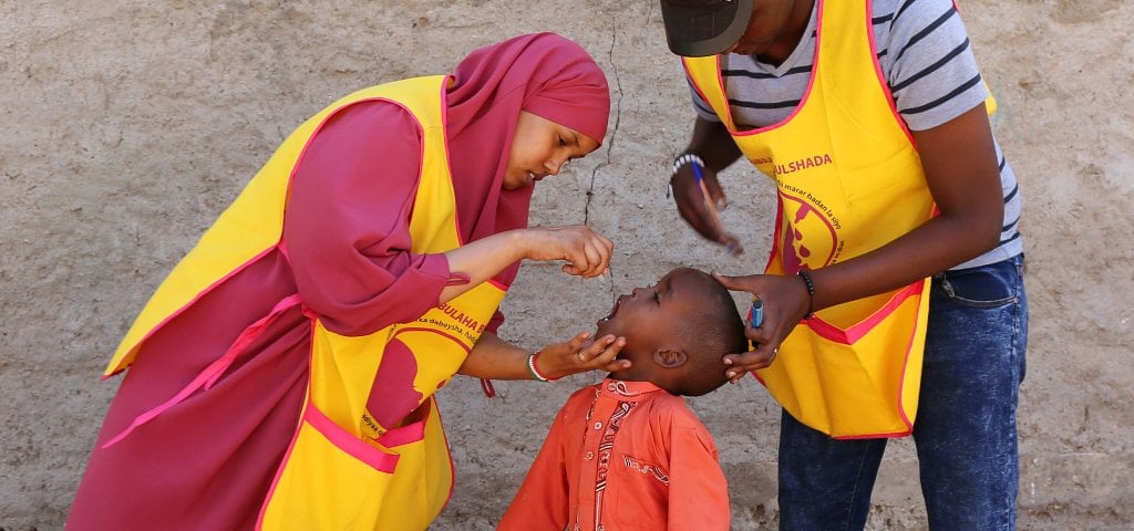A member of a volunteer vaccination team provides oral polio vaccine to a child.