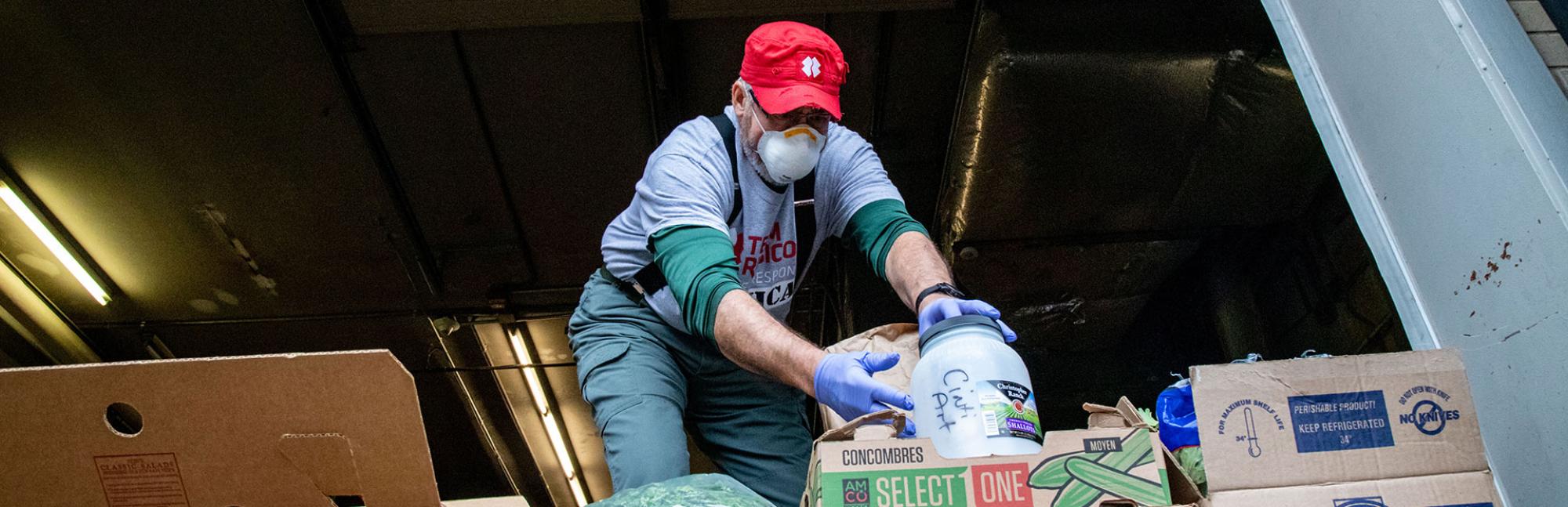 Masked volunteer unpacks boxes of redistributed food from lorry