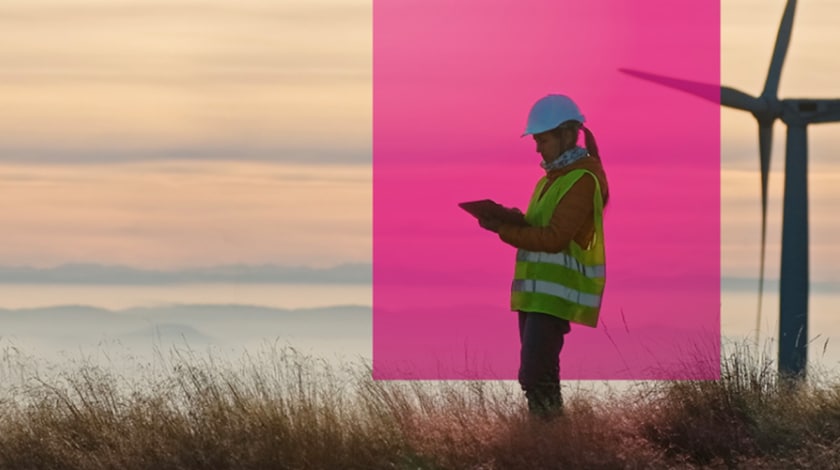 A wind energy engineer checks her ablet on a wind farm at dawn.