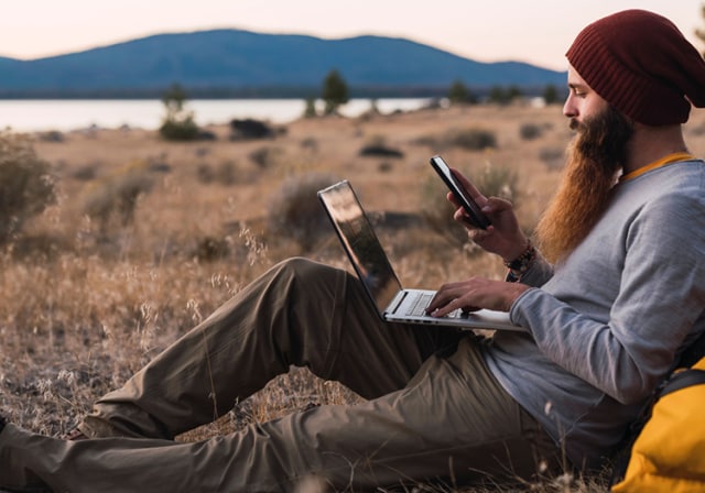 A man connecting to internet in the wilderness via a hotspot device.