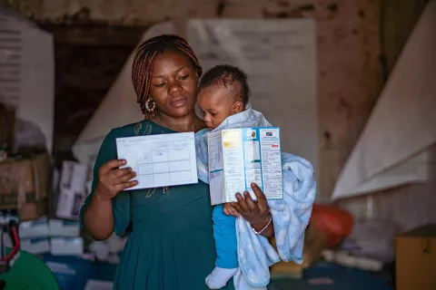 A mother holds holds two vaccination records and a baby.