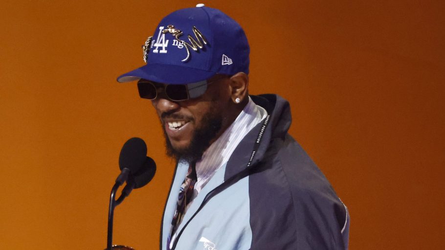 Kendrick Lamar at 65th Grammy Awards, wearing a grey and baby blue jacket, Blue hat, and Black shades.