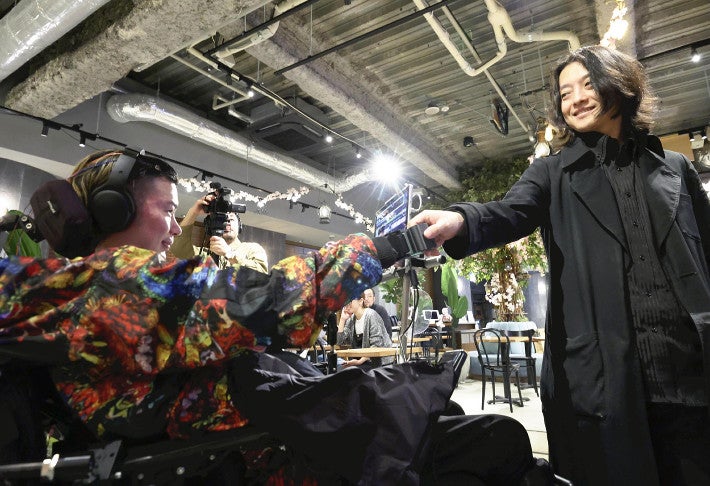 脳波でロボットアームを操り、握手を交わす武藤さん（左）（東京都内で）