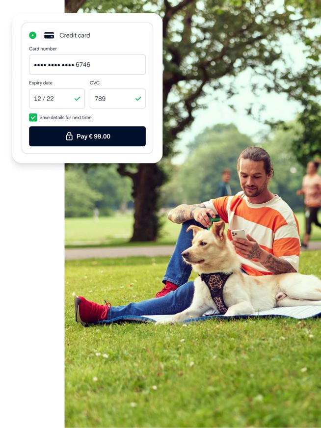 Man sitting down in park next to his dog, he is making an online payment on phone