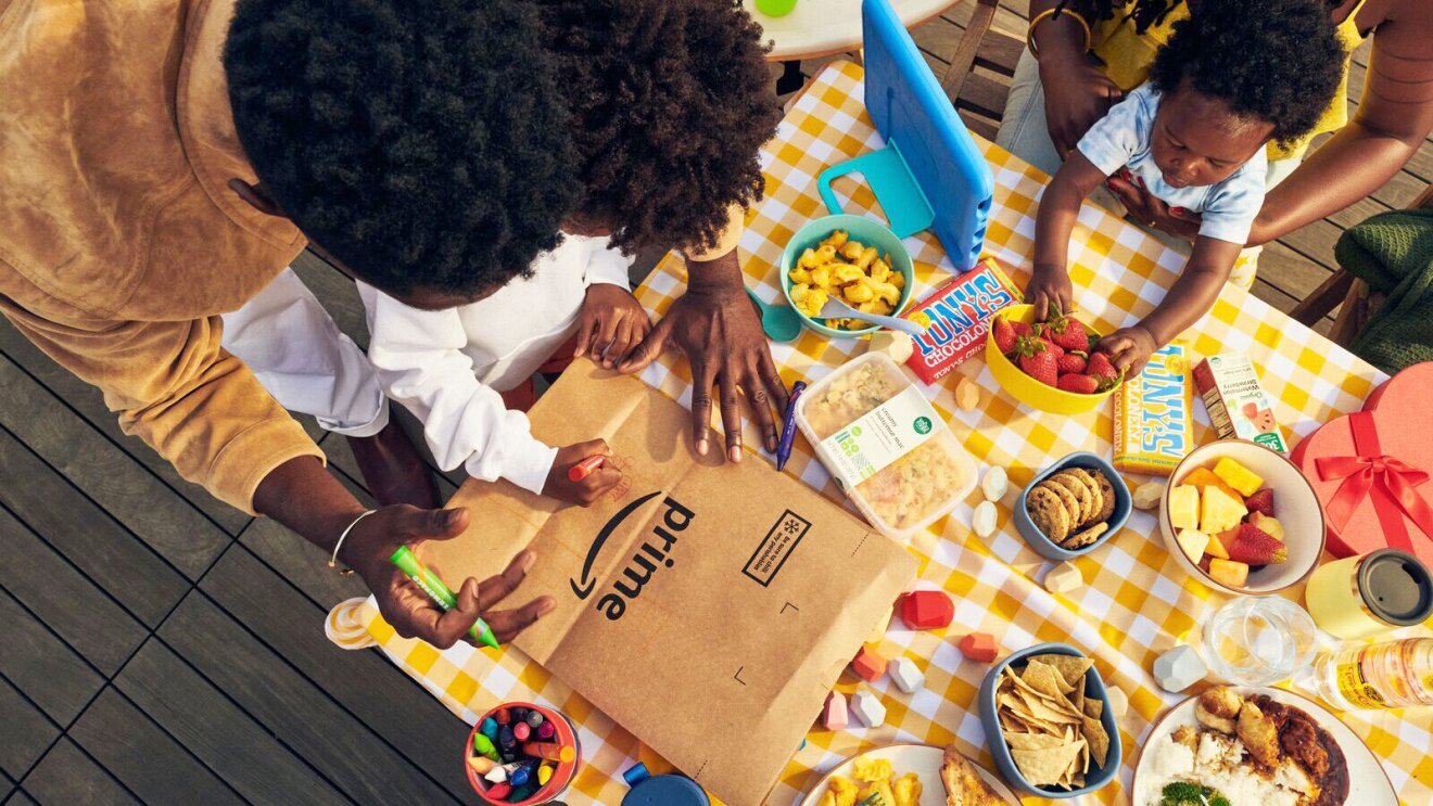 An image of a table full of food. There are two children sitting at the table with their parents. One parent is helping one child color on an Amazon box.