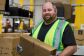 A photo of an Amazon fulfillment center employee holding an Amazon delivery box inside a fulfillment center.