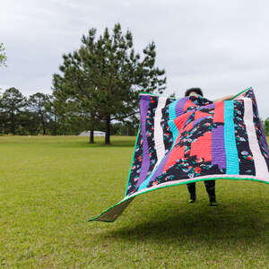 woman holding quilt from gee's bend quilting collective in alabama while standing in a field