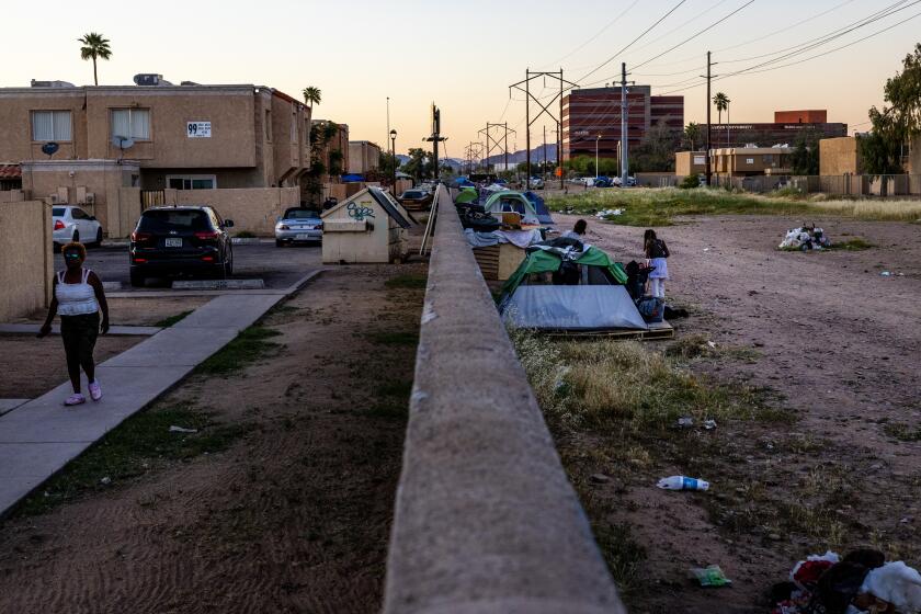 A homeless encampment the length of a city block butts up against a stucco wall with an apartment complex on the left side