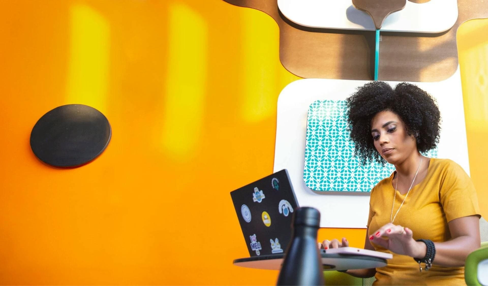 Mujer trabajando en computadora frente a un fondo amarillo.