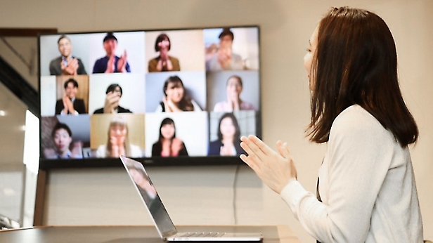 モダンなオフィスで大画面に表示されたビデオ電話会議を通じて同僚にプレゼンテーションを行っている女性。